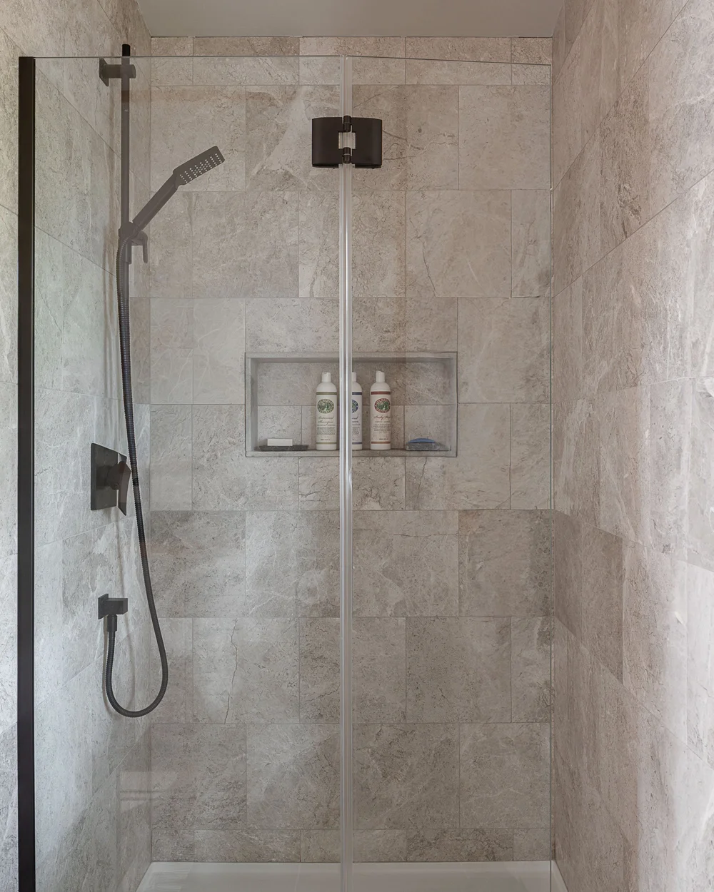 A tiled shower with a glass door, a recessed niche in the back wall