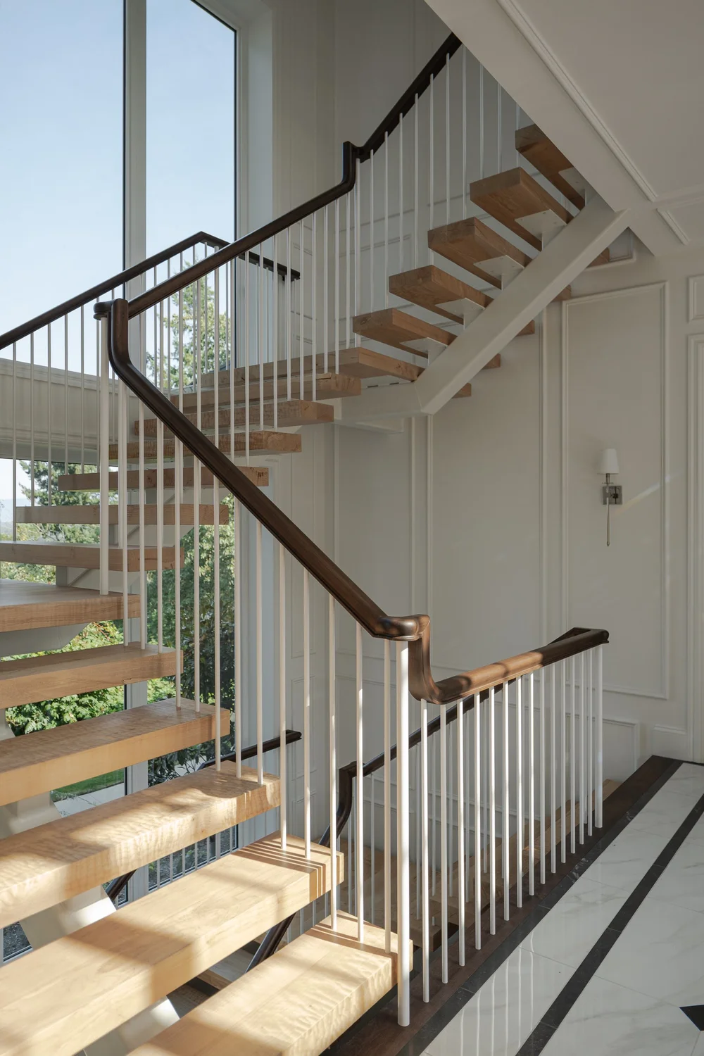 Wood treads winding up past slim white spindles and a dark handrail beside tall glazing