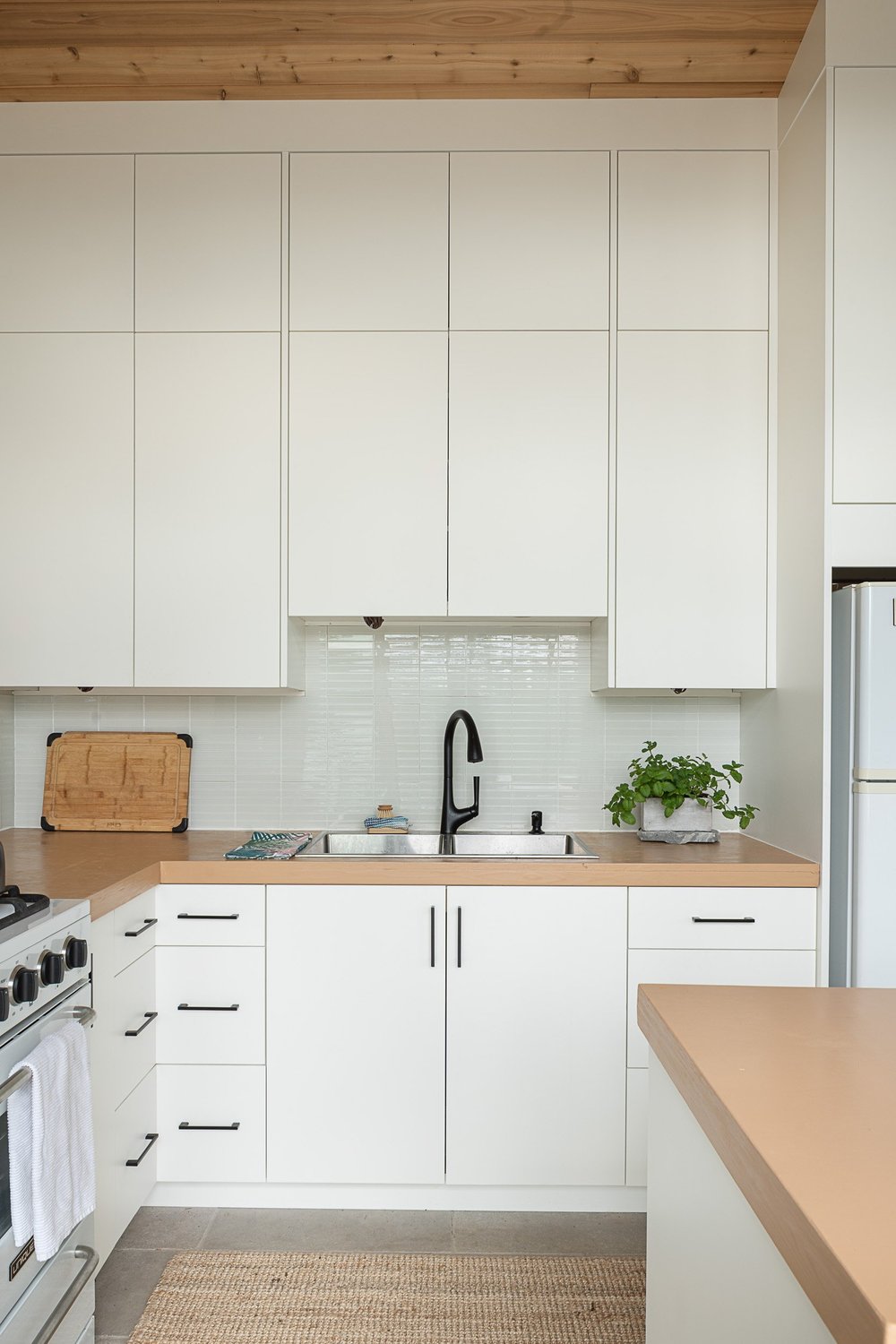Kitchen elevation with white cabinets to the ceiling, a sink and a black tap