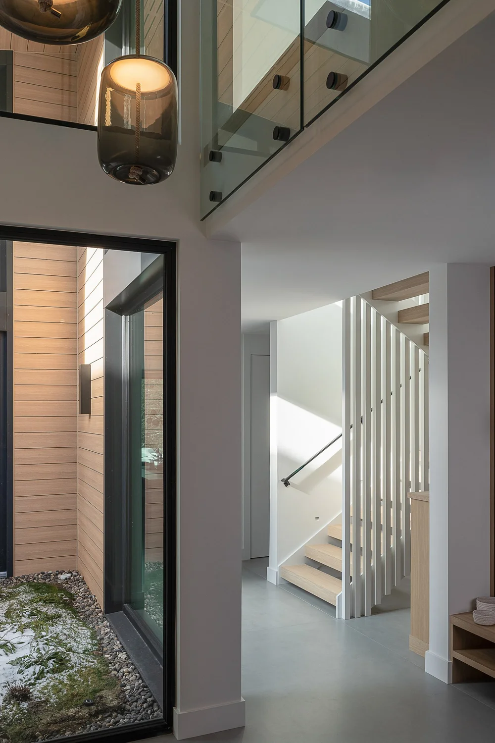 Double height hall beside a glazed light court, a pendant above and the stair beyond