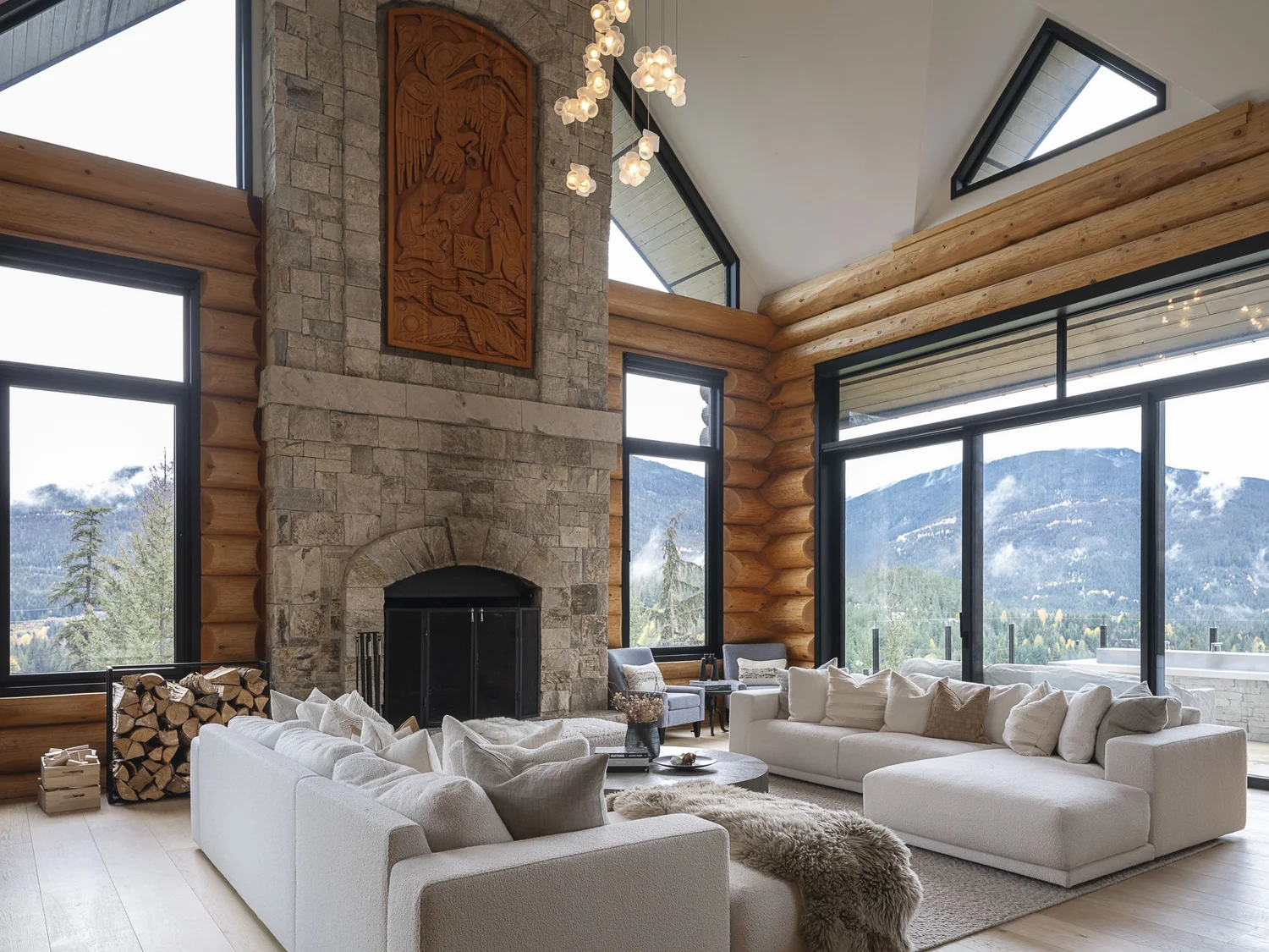 Living room with two white sofas facing a stone fireplace, mountains through the windows at right