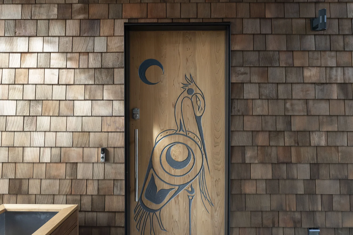 A wood entry door carved with a bird and moon motif in a shingled wall