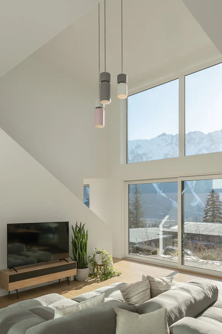 Double height living room with pendant lights and glazing onto snow covered mountains