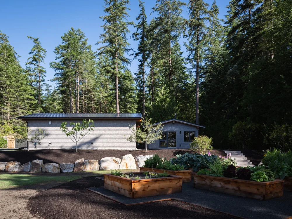 Outbuildings beyond raised timber beds, boulders set along the edge of the lawn