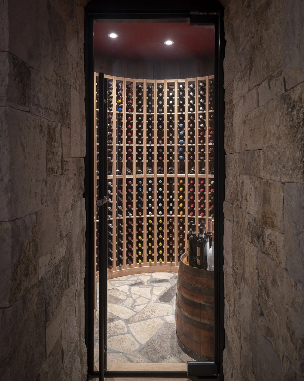 Glass door onto a wine room, racking floor to ceiling and a barrel on stone paving