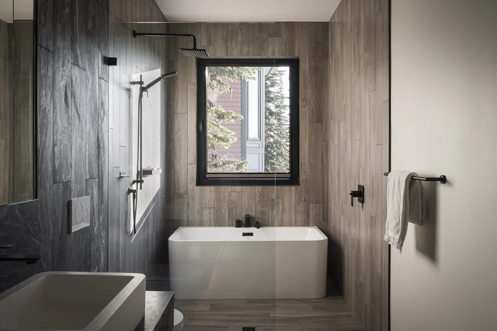 White freestanding tub under a window, dark stone shower to the left