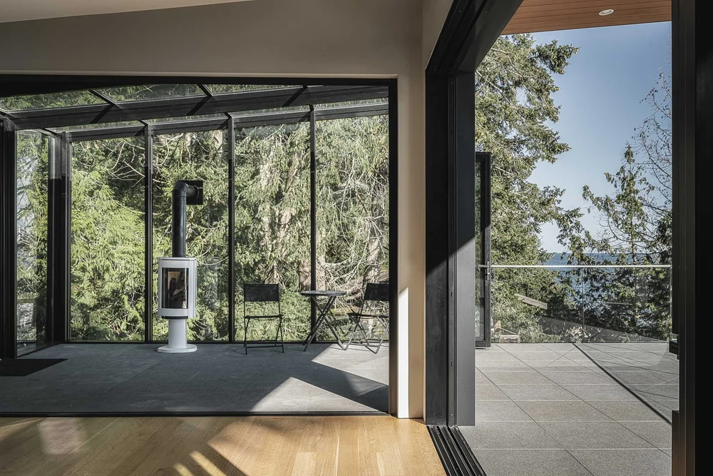 Looking through to a glazed room with a freestanding stove, terrace and water at right