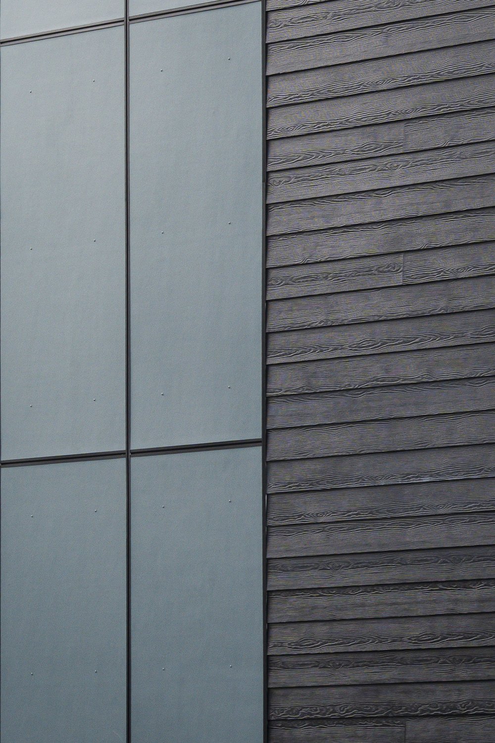 Cladding detail, a flat grey panel meeting dark board siding with a deep grain