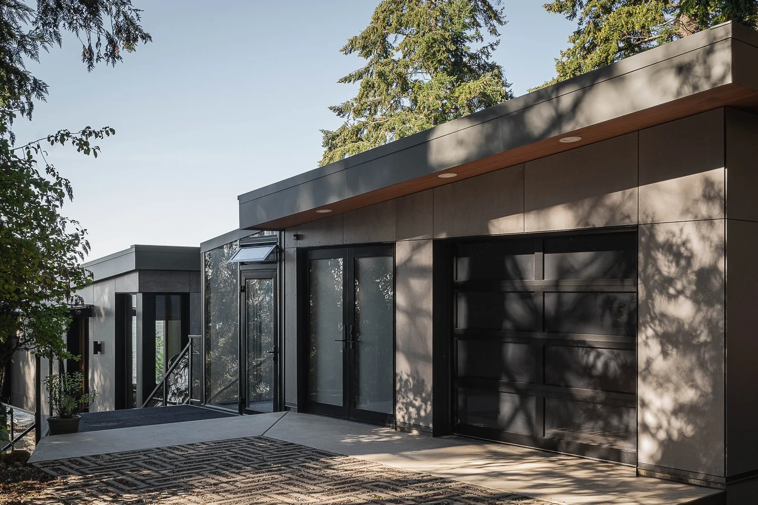 Entry elevation in dark panel cladding, a glazed vestibule beside a wide garage door