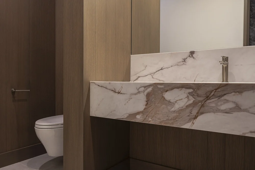 Powder room with a veined stone counter folded down over dark cabinetry, wall hung toilet beside