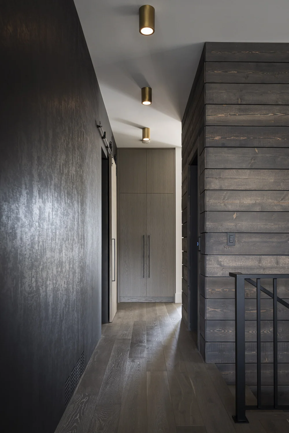 Corridor in dark wood with ceiling spots, cabinetry ahead and a stair rail