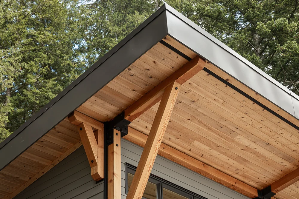 Roof edge from below, wood soffit boards and a braced post against a dark fascia