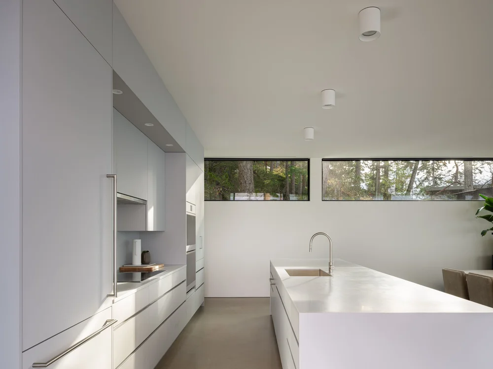 Counter and sink under a ribbon window, tall cabinetry running the length of the wall