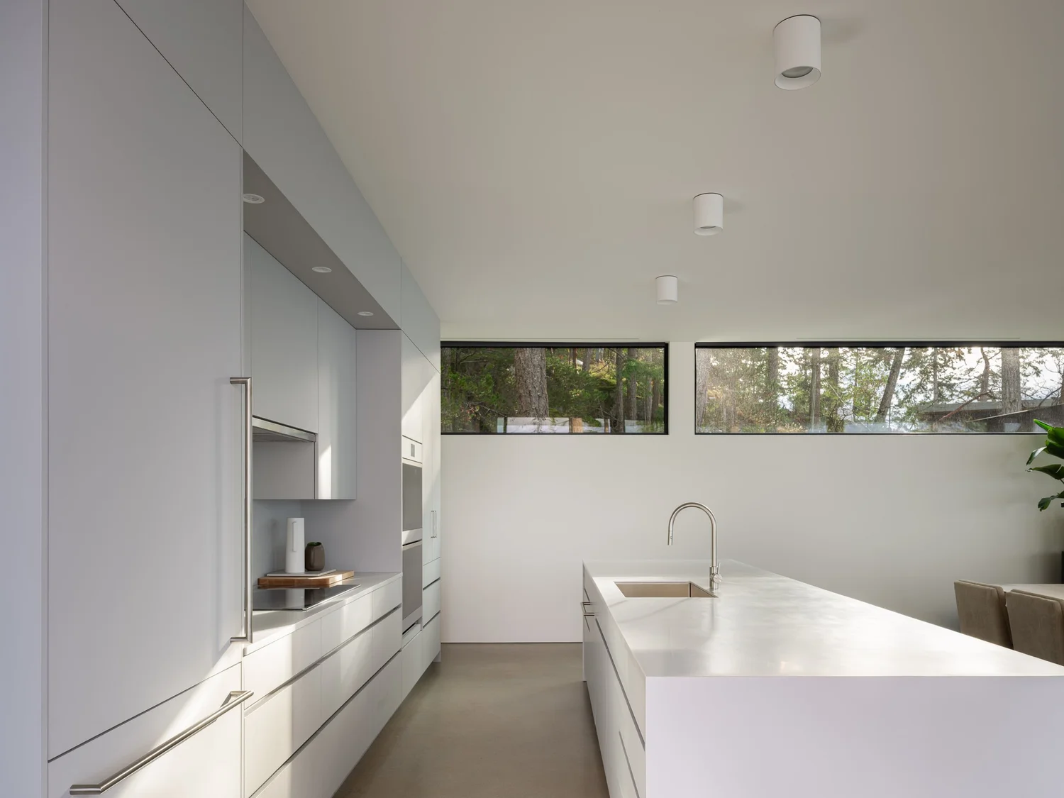 Counter and sink under a ribbon window, tall cabinetry running the length of the wall