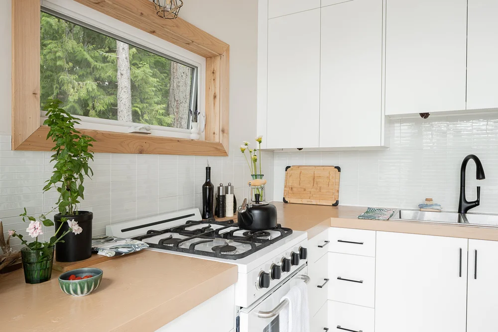 A gas range beside a counter, an awning window in a wood frame above the backsplash
