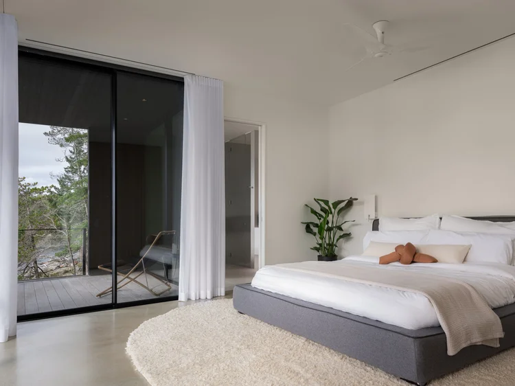 Bedroom with a black framed sliding wall open to a deck, white bed and a round rug