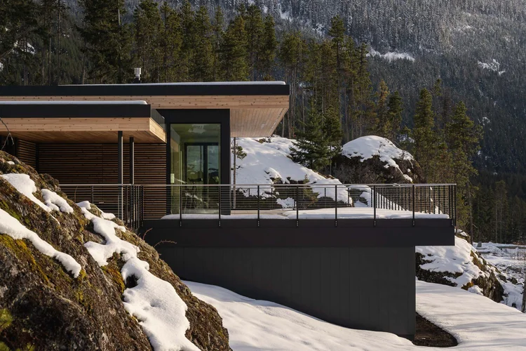 The house along the rock outcrop, dark cladding under a pale wood soffit with snow below