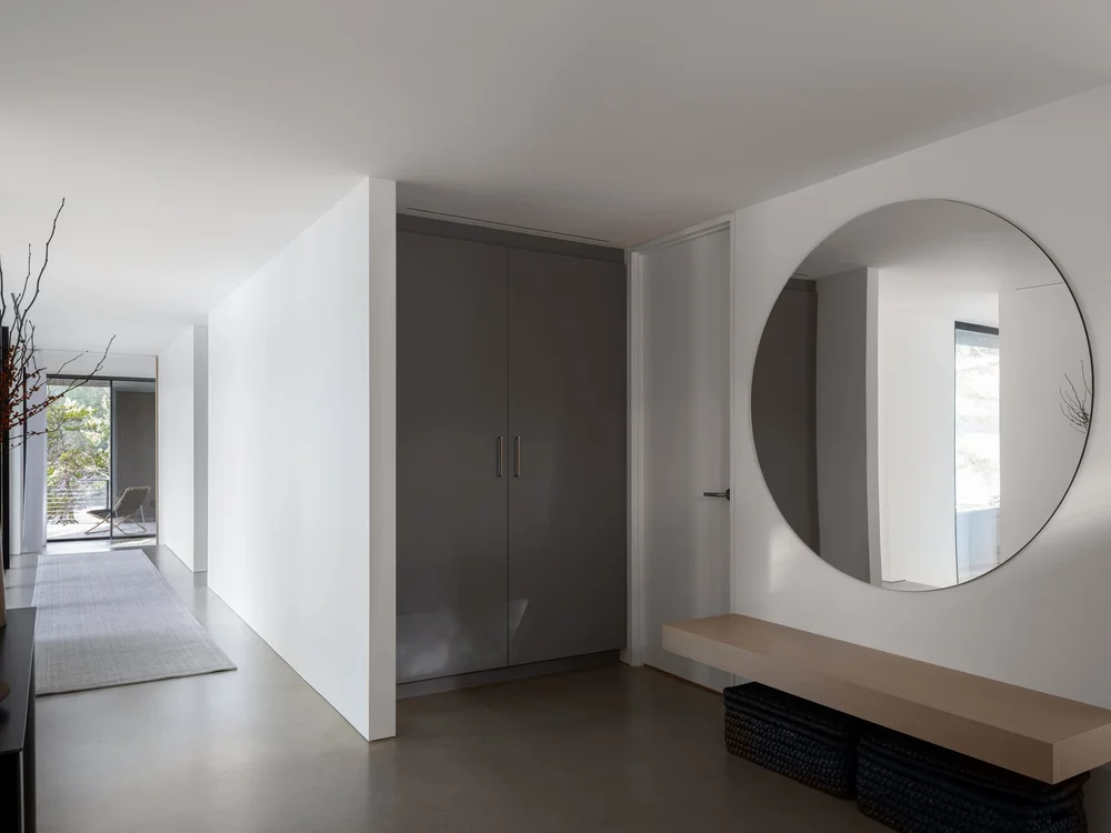 Hall with a large round mirror above a floating bench, tall doors and baskets below
