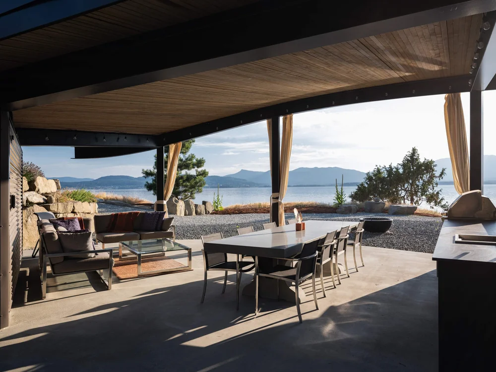 Under the pavilion roof, a long table and lounge chairs open to the water