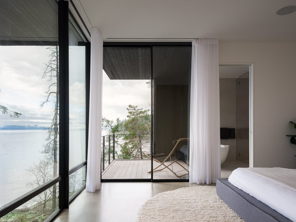 Bedroom opening to a deck with a folding chair, the water and an ensuite beyond