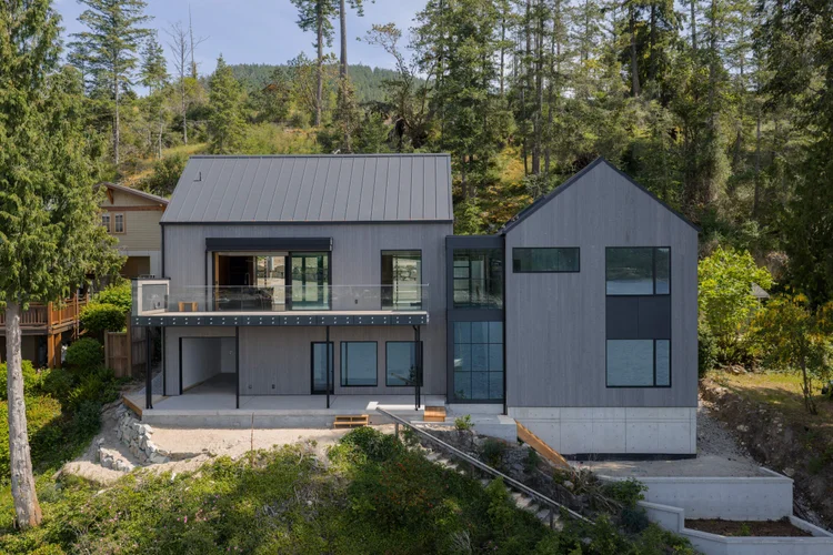 Two grey gabled volumes joined by a glazed link, set on a concrete base above the shore