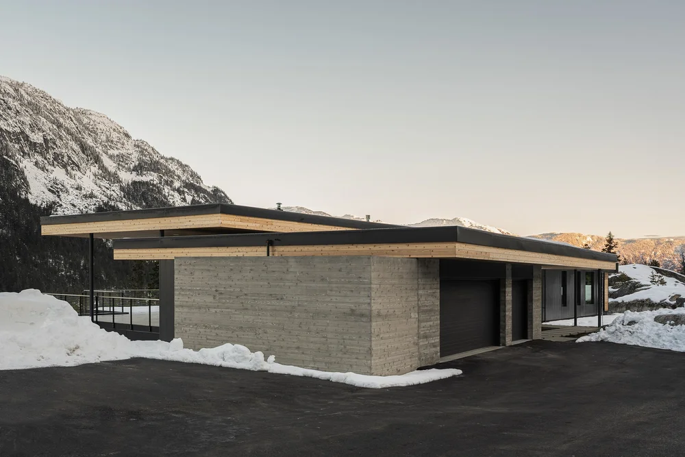 Entry elevation in low light, a long roof plane over a pale textured wall