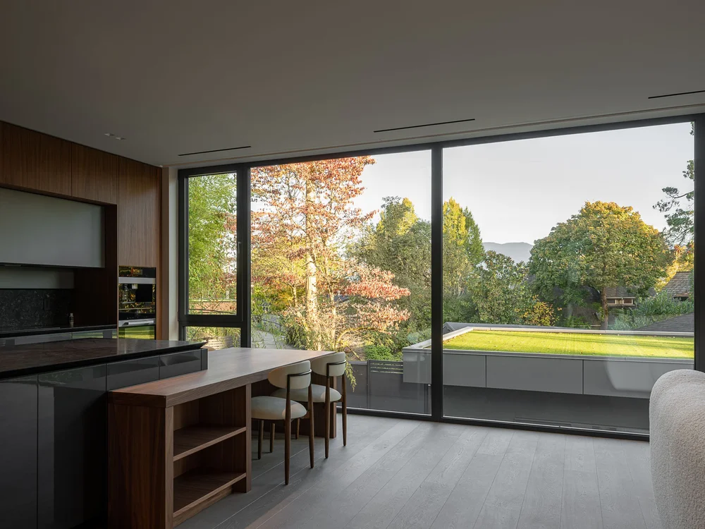 Kitchen and table looking out to autumn trees, a grass roof and distant mountains