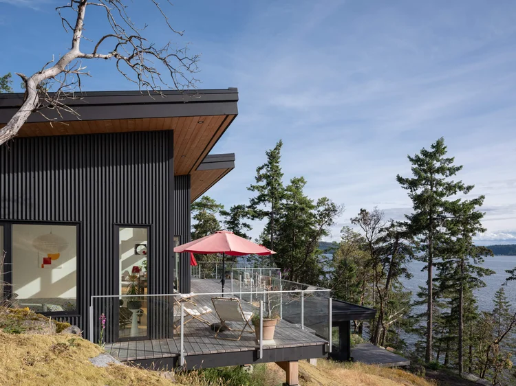 Oles Cove, Halfmoon Bay, dark corrugated cladding and a deck with a red umbrella above the ocean