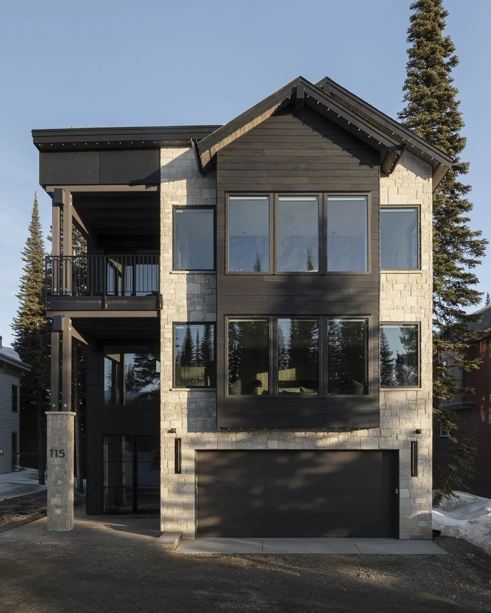 Front elevation in low sun, stone base and dark siding under a steep gable