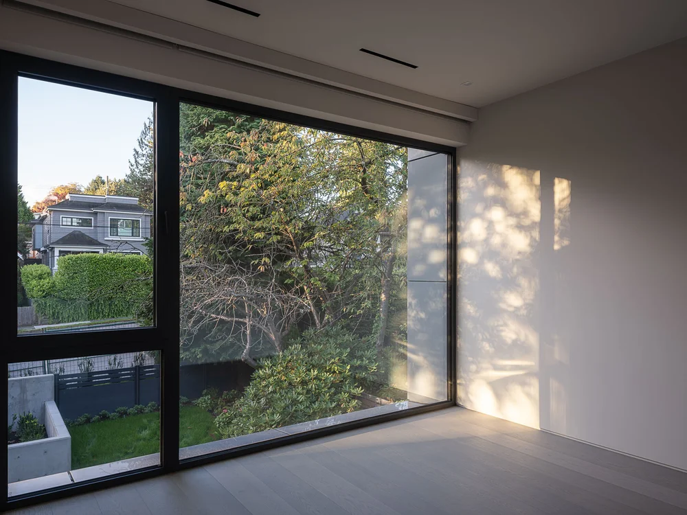 Corner glazing to the garden and hedge, dappled light across the end wall