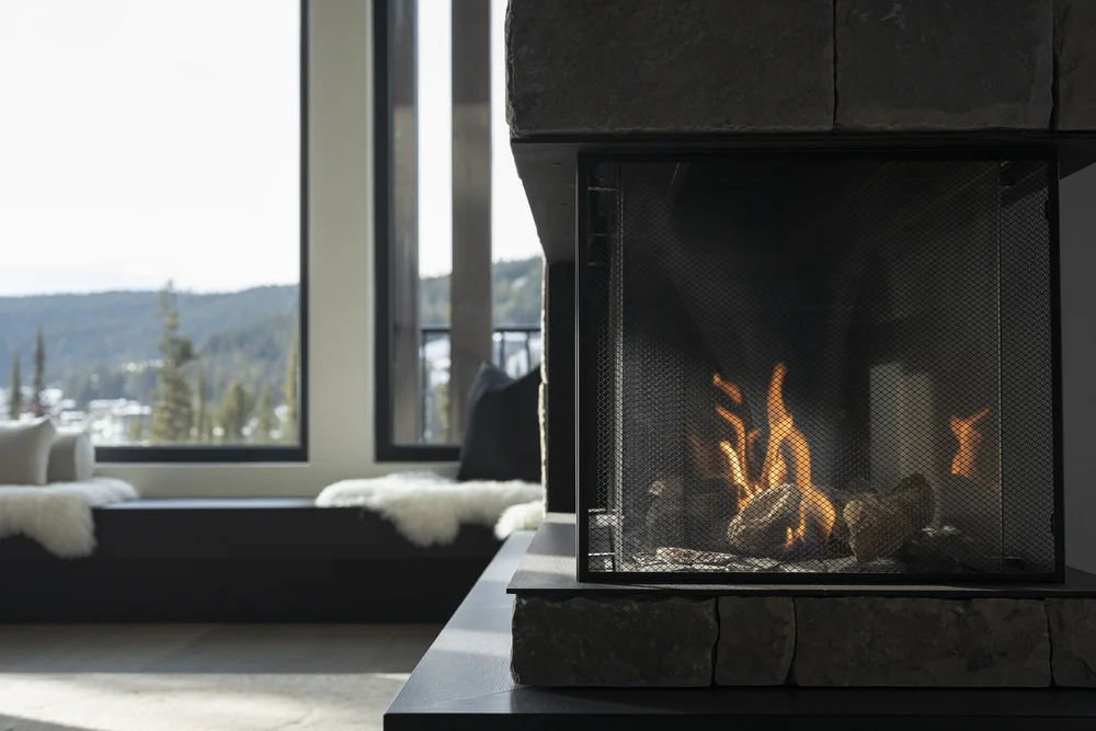 Fire burning in a black firebox beside a window seat, snowy hills beyond