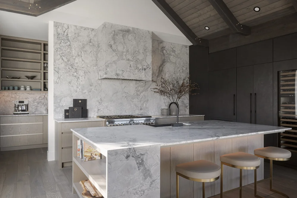 Kitchen with a veined stone hood wall and island, dark cabinetry to the right