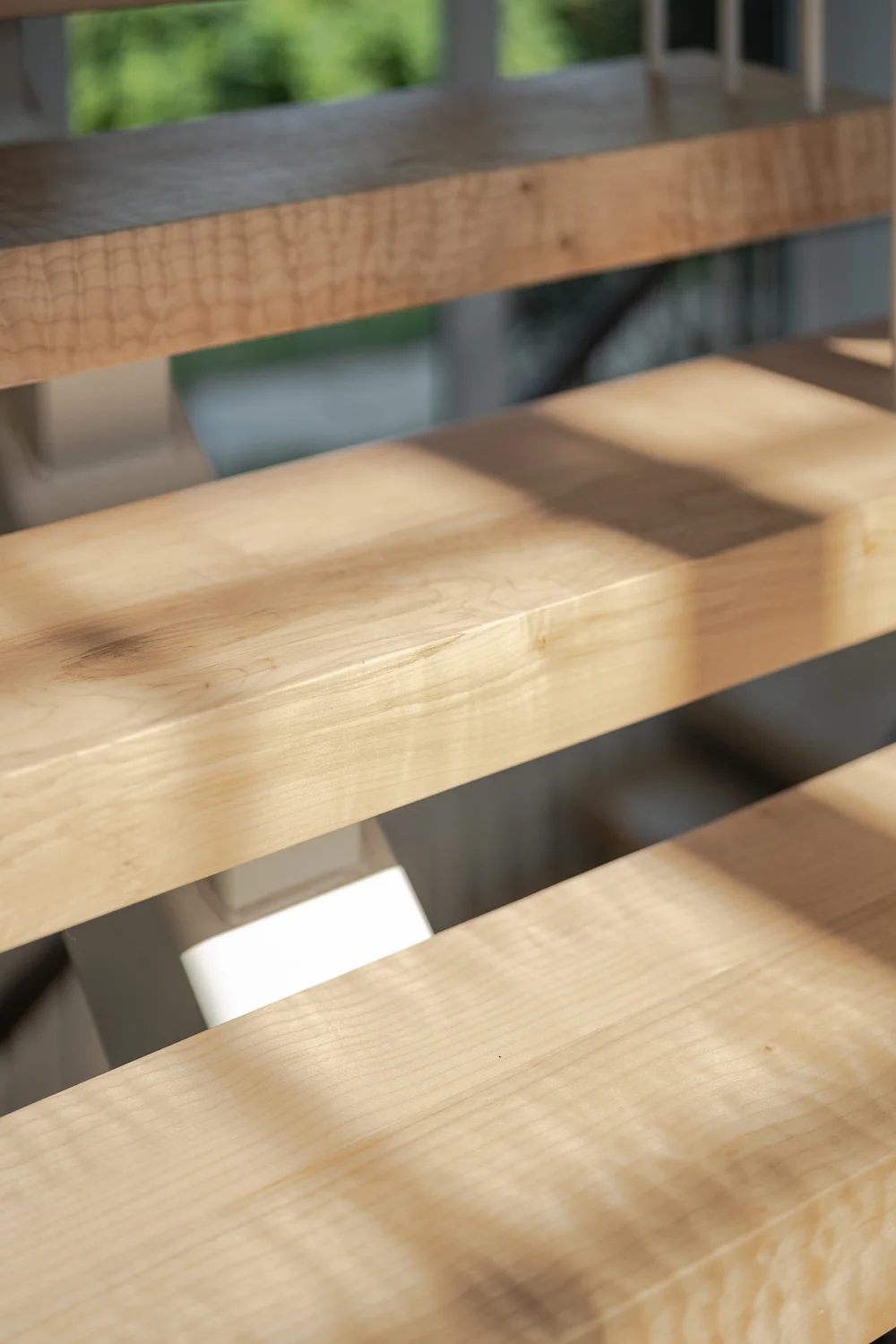 Close on figured wood stair treads with sunlight raking across the open risers