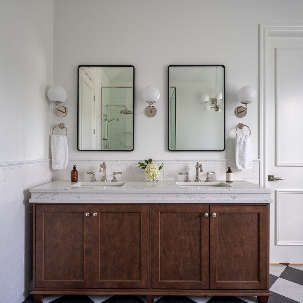 Double vanity in dark wood below two black framed mirrors and globe sconces