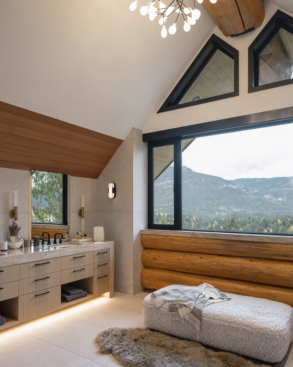 The primary bathroom under a sloped wood ceiling, the vanity facing a window to the mountains