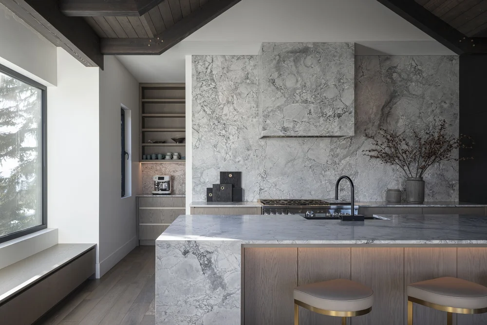 Kitchen seen past a window bench, the stone island running the length of the room