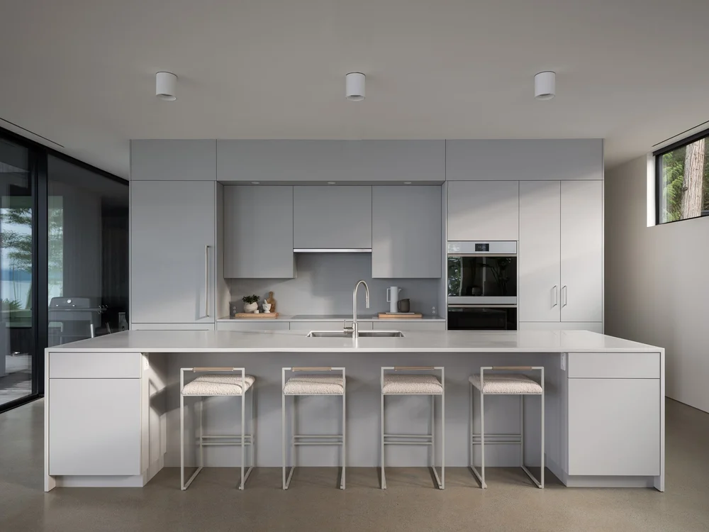 White kitchen island with four stools, wall ovens and full height cabinets behind