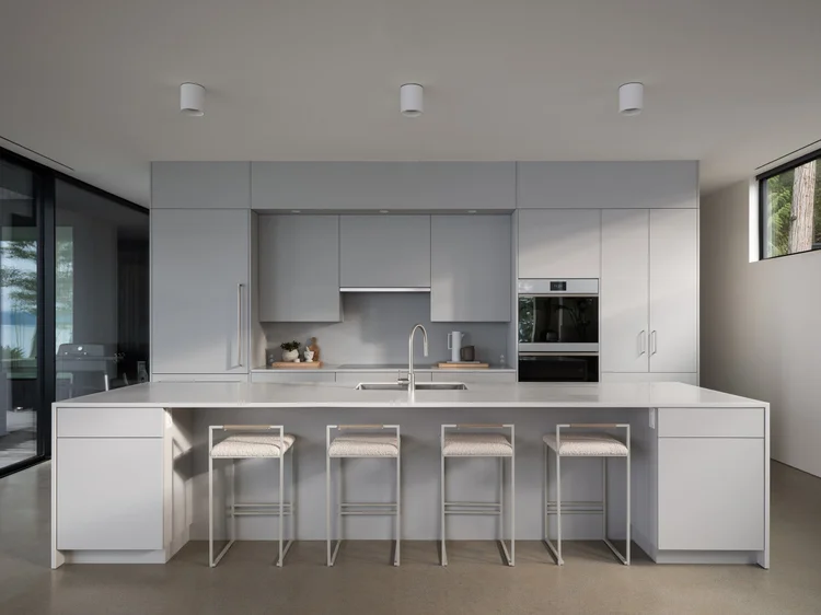 White kitchen with a long island, four stools and integrated ovens