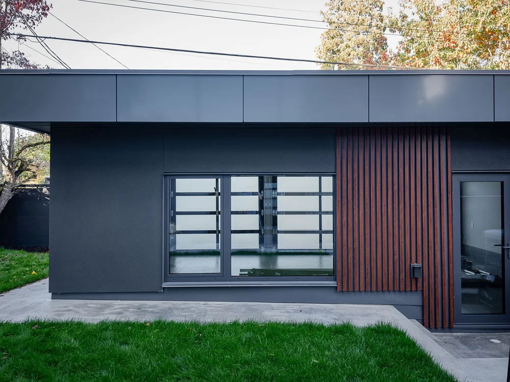 Low outbuilding in dark cladding with a slat panel, window through to the garage