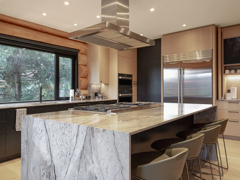 The island end where the stone top folds to the floor, cooktop and hood beyond