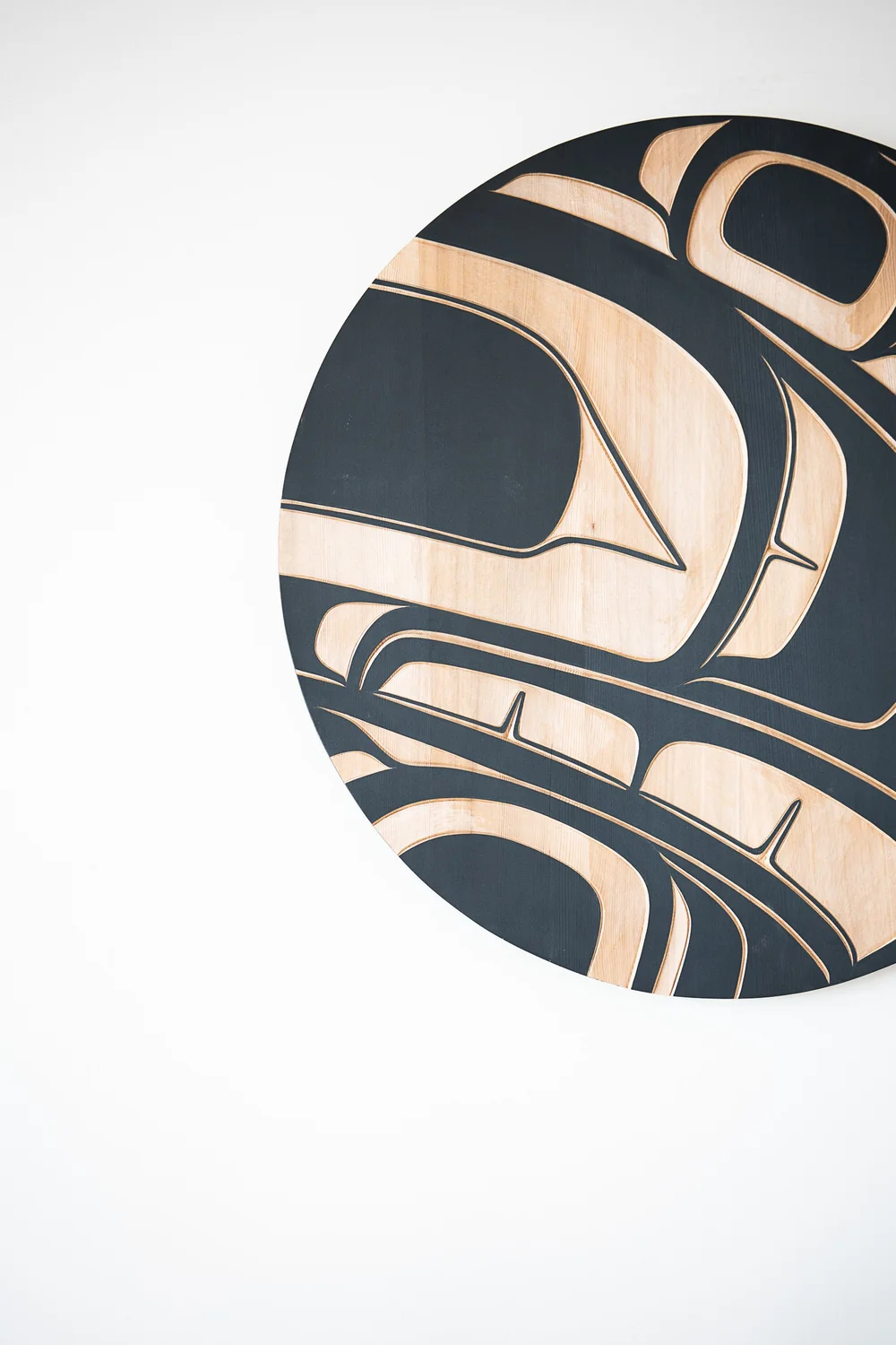 A circular wood panel with a black and pale carved design on a white wall