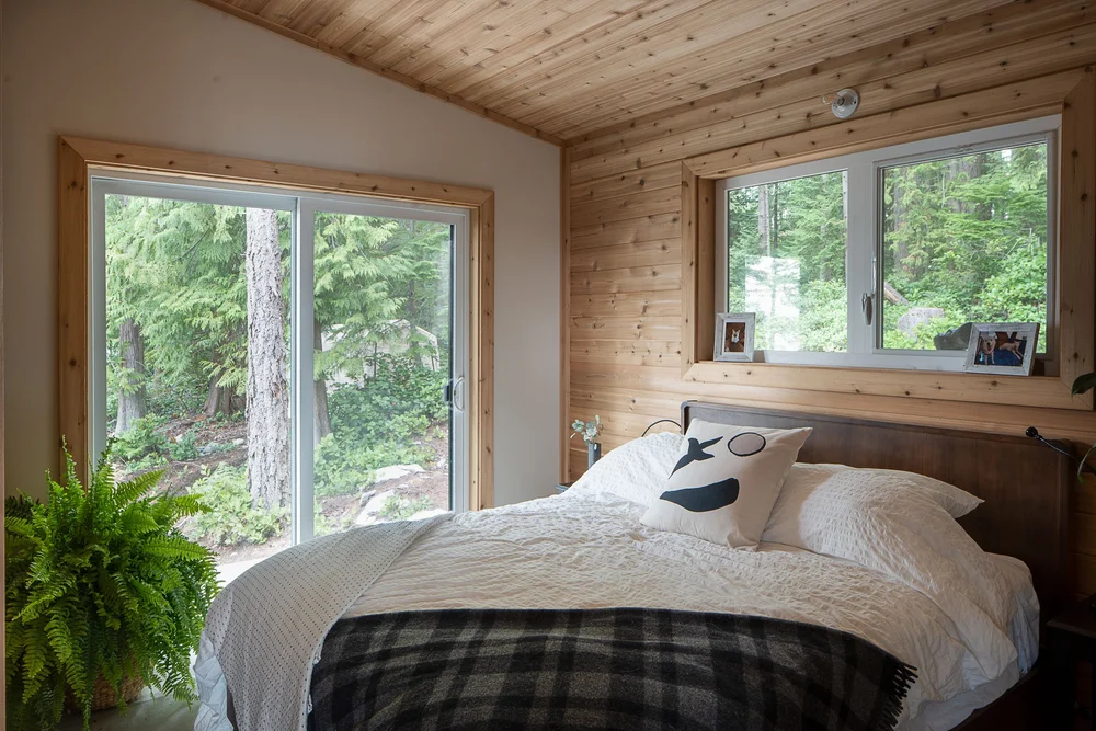 Bedroom with sliding glass to the forest, a plaid blanket across the bed