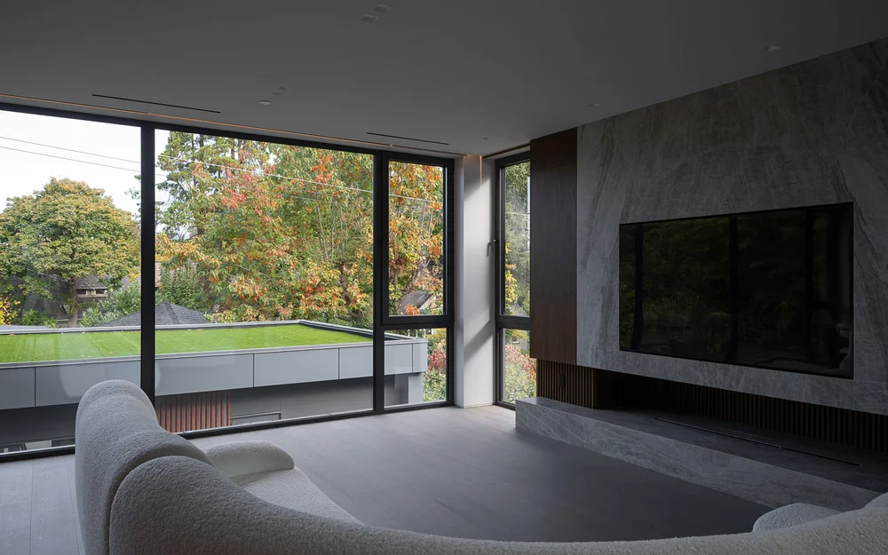 Living room from behind the sofa, stone fireplace wall and corner glazing to the grass roof