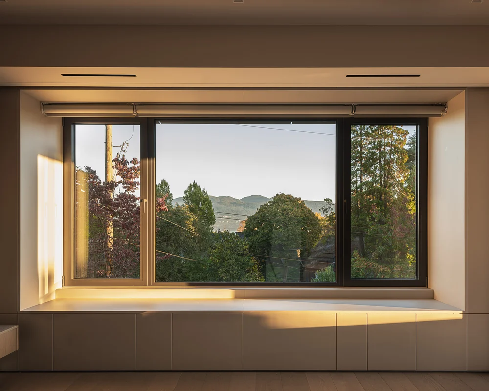 Evening light across the wall above the window seat, trees and a ridge outside