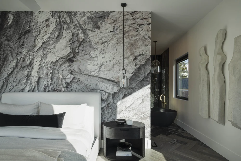 Bedroom opening through to an ensuite, a dark tub and pale wall sculptures beyond