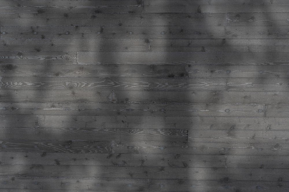 Dark stained horizontal siding in raking light, branch shadows across the boards
