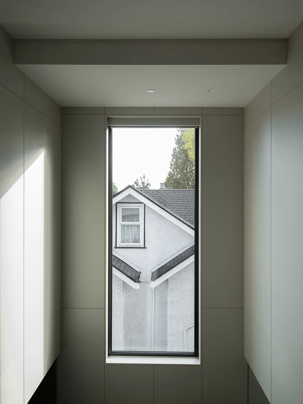 A tall slot window at the end of a pale panelled passage, a neighbouring gable beyond