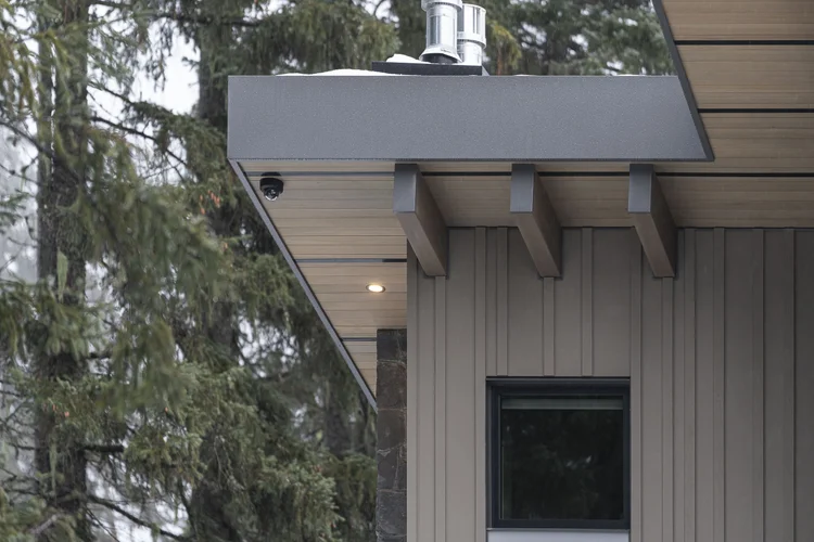 Deep roof overhang on exposed beam tails at a building corner, a tall evergreen alongside