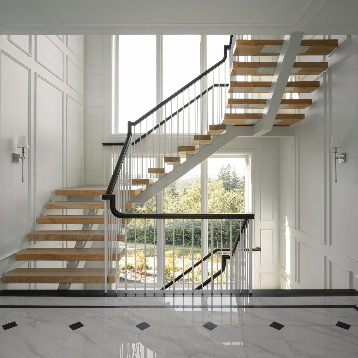 Open stair with wood treads against a two storey window looking out to trees and hills