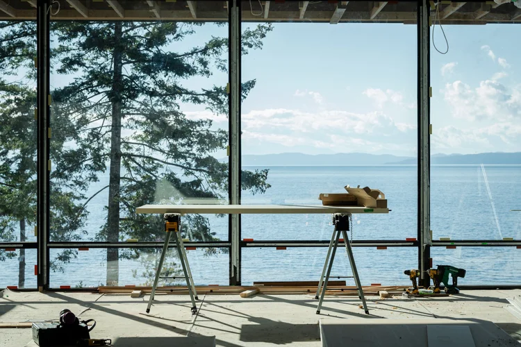 Construction tools on a sawhorse, ocean and mountains through full height glass beyond